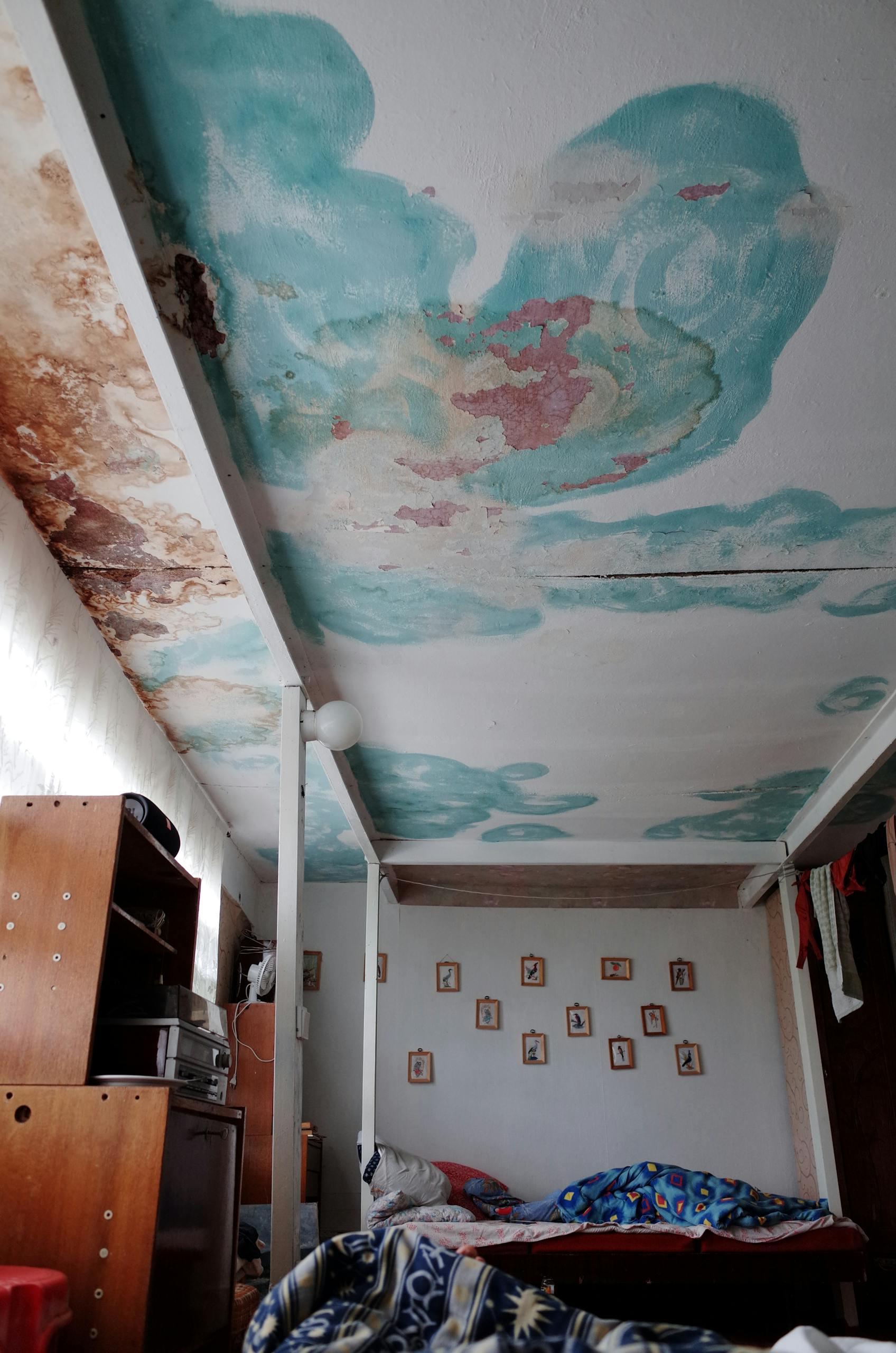 An old bedroom featuring unique ceiling art with peeling paint and vintage furnishings.
